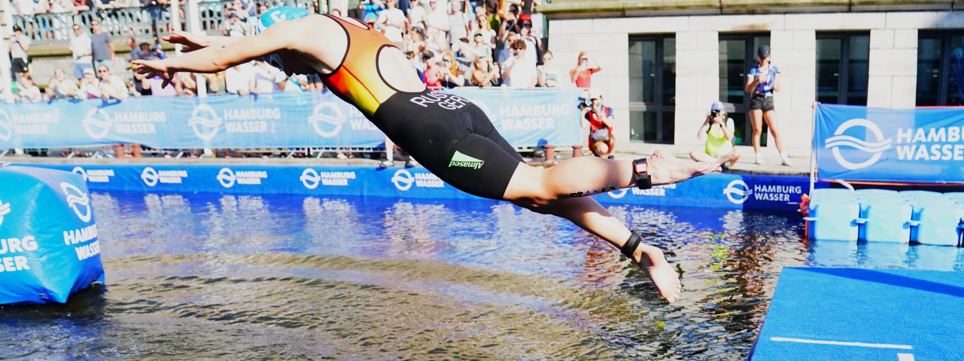 Ein deutscher Elite-Athlet springt beim Start in die Alster – im Hintergrund die Zuschauer beim Suzuki World Triathlon Hamburg.