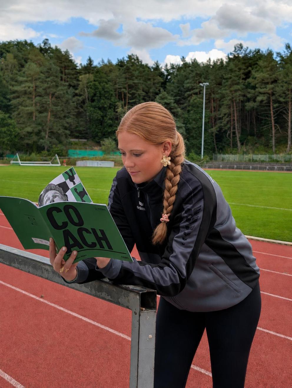 Eine junge Athletin liest auf der Laufbahn die NADA-Broschüre „Coach“.